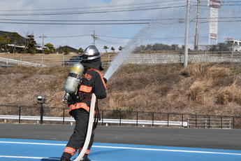 消防署の敷地内で、消防車に繋いだホースを持ち放水する、装備した隊員１人の後ろ姿